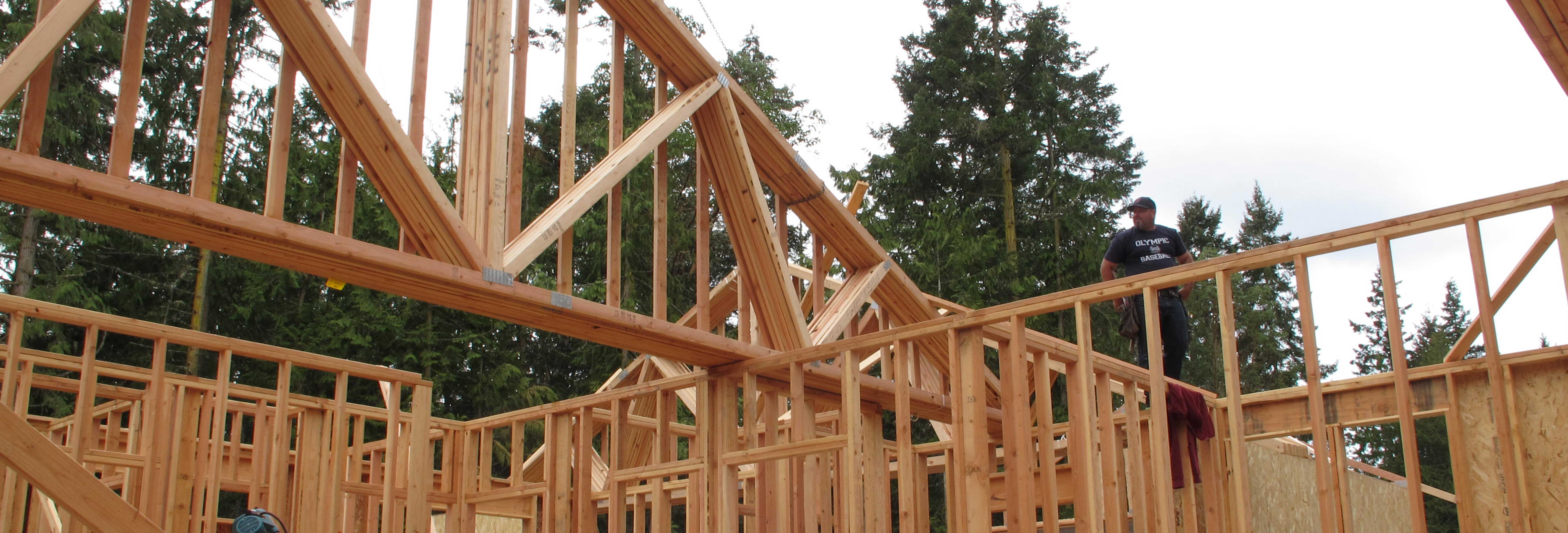 Custom Homes - Carpenter guiding roof truss from crane to wall frame on house under construction